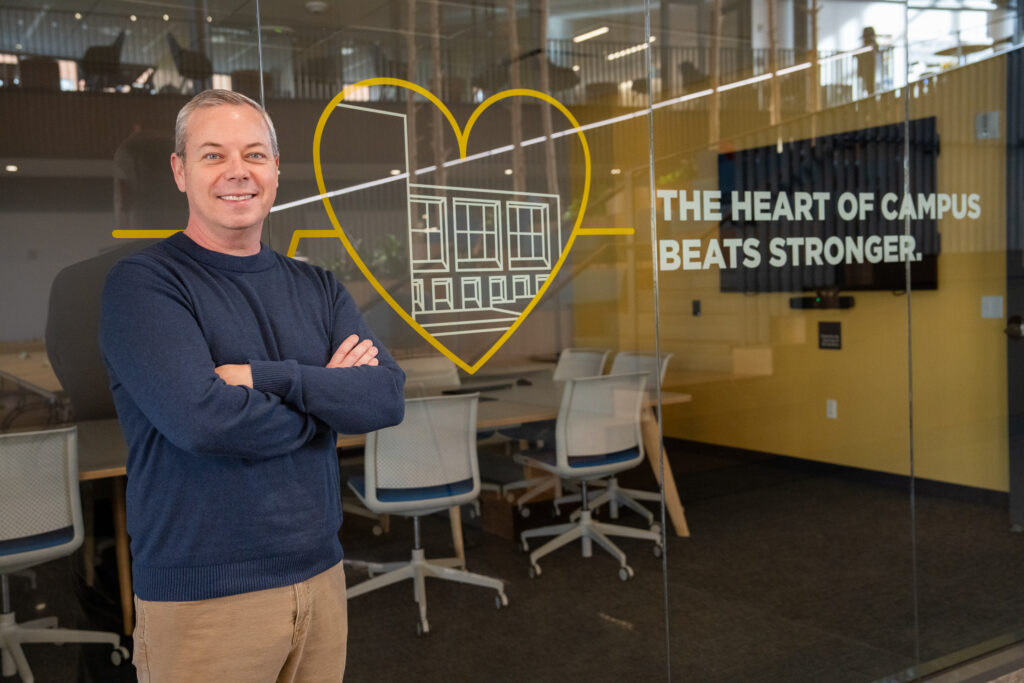 Bill Y, online bachelor's in respiratory therapy student, standing with arms crossed and smiling in front of "The Heart of Campus Beats Stronger" graphic.