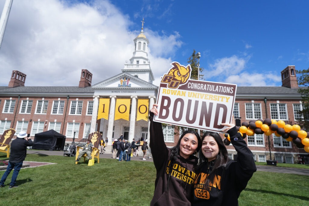 Two students smiling at Rowan University's Accepted Students Day with a 'Rowan University Bound' sign.
