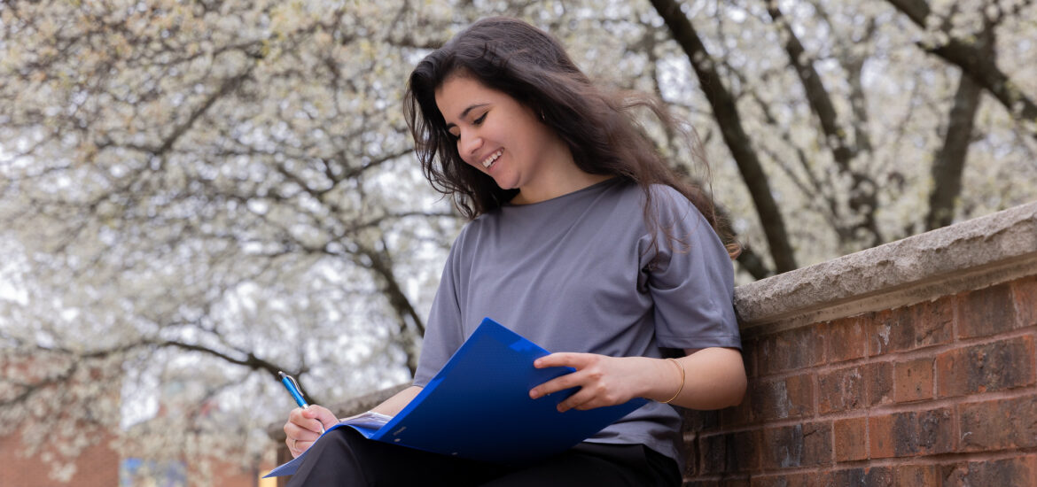 Woman sitting outside with blue folder and notepad reviewing MBA coursework while planning career growth.