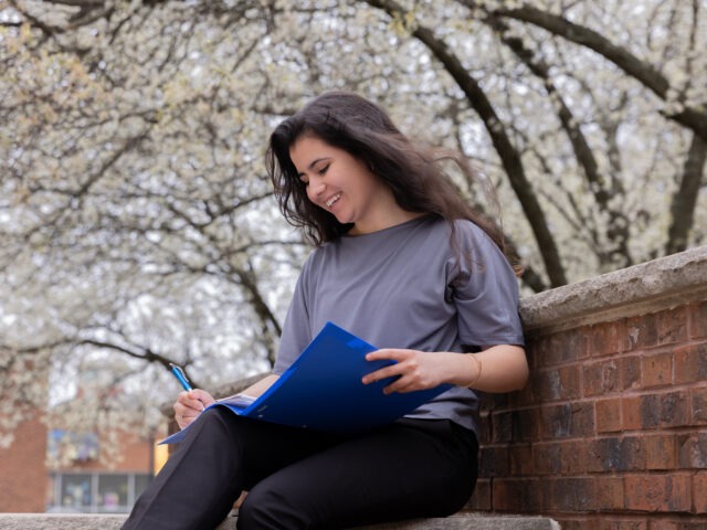 Woman sitting outside with blue folder and notepad reviewing MBA coursework while planning career growth.