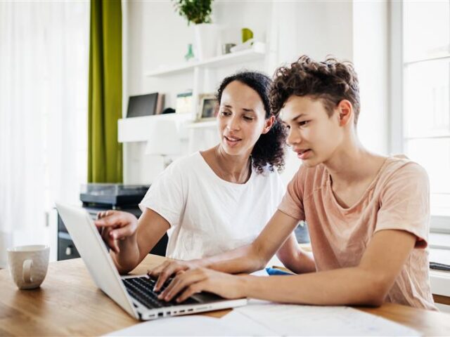 Mother sitting with high school senior son on laptop, providing guidance and support through the college decision-making process.