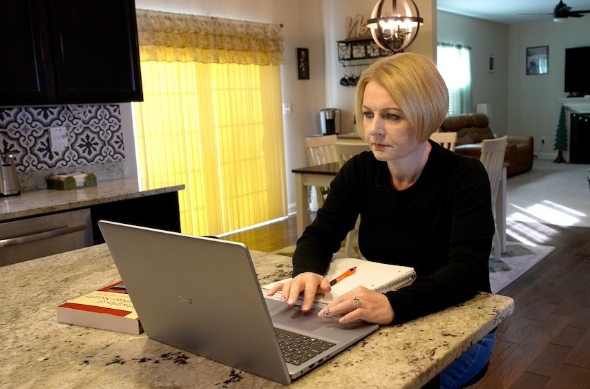 Rowan online master's in cybersecurity student Jennifer  works at her laptop at her kitchen island. 