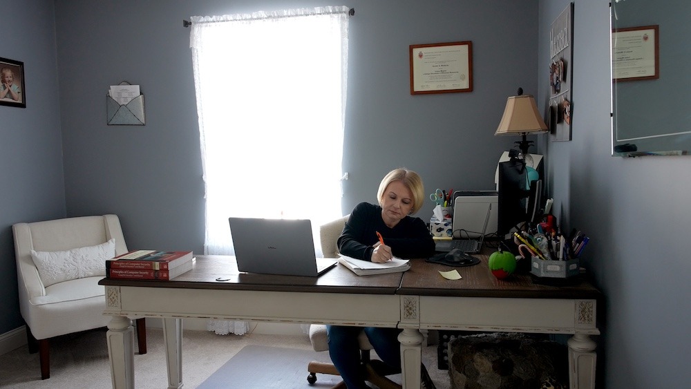 Rowan online master's in cybersecurity student Jennifer writes in a notebook in her home office, which feels warm and inviting. 