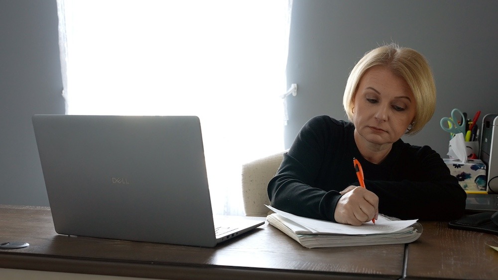 A close up of Rowan online master's in cybersecurity student Jennifer as she writes in a notebook in her home office. 