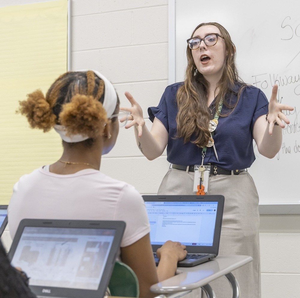 Sarah Busch stands at the front of a classroom, captured in mid-lecture talking with her hands extended.