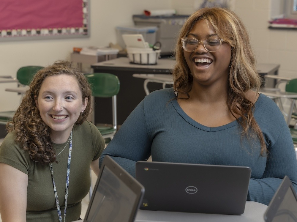 Kellianne O'Neill crouches next to a student's desk.