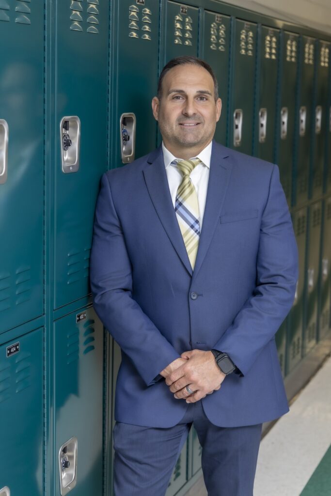 Kurt Marella slightly leans against the lcokers, his hands clasped in front of him.