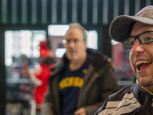 Rowan master's of special education alumnus Josh Schneider turns slightly to the right, smiling as he is speaking to someone. He is wearing a hockey uniform, glasses and a baseball cap.