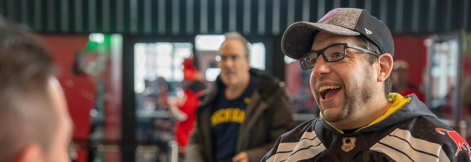 Rowan master's of special education alumnus Josh Schneider turns slightly to the right, smiling as he is speaking to someone. He is wearing a hockey uniform, glasses and a baseball cap.