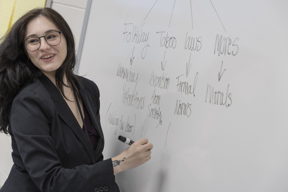 Raya Slotoroff looks over her shoulder slightly, to the classroom, as she writes on the board.