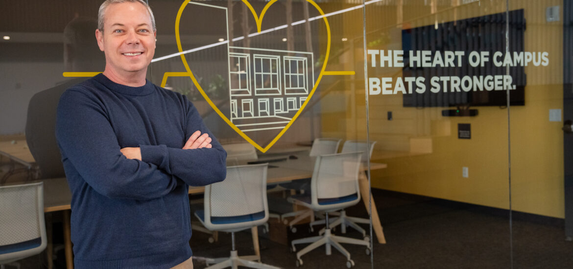 Bill Y., Rowan Online Bachelor of Respiratory Therapy student, smiling in front of a graphic that says 'The Heart of Campus Beats Stronger.' with arms crossed.