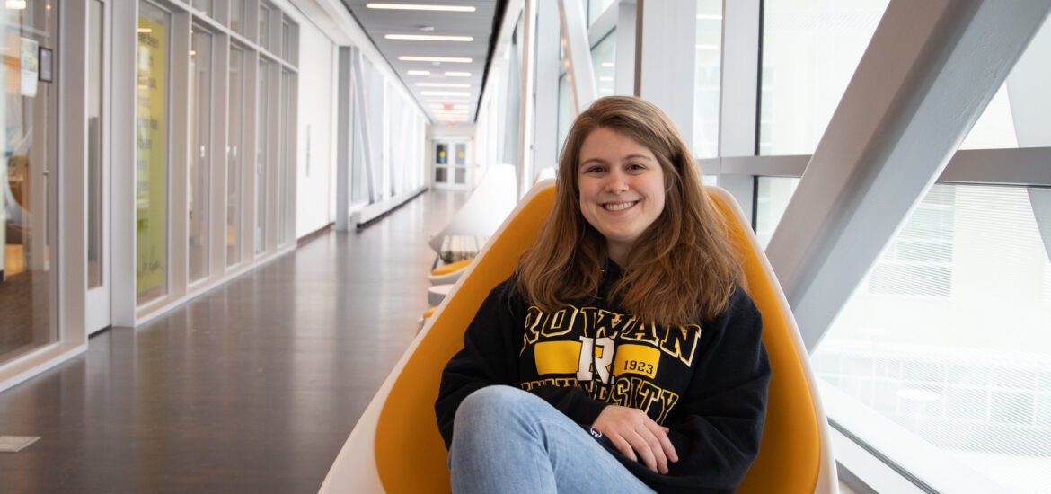 Female student sitting in a chair in Rowan University's engineering hall smiling.
