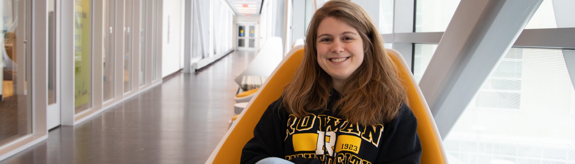 Female student sitting in a chair in Rowan University's engineering hall smiling.