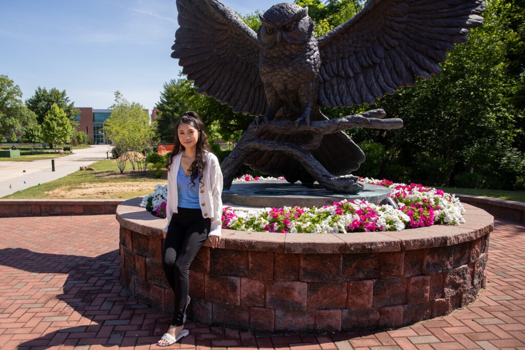 Student thinking about enrolling in a summer course at Rowan standing by owl statue outside.