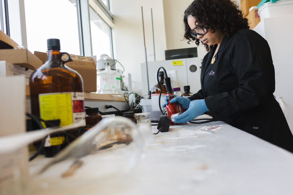A Rowan University student holds a device, while working carefully at a table in a lab. 