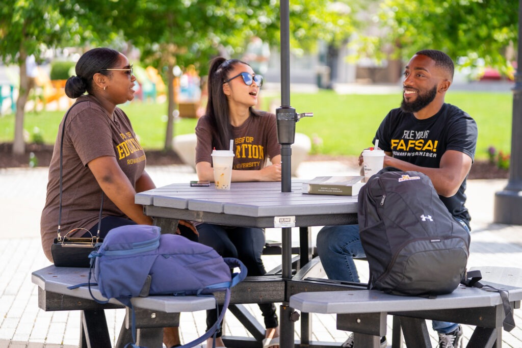 Students enrolled in summer college courses sitting outside talking at a table with their backpacks.