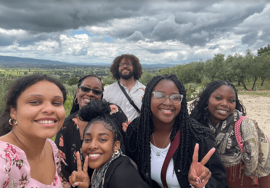 Layahna W. stands in a group selfie with friends in Italy, with the landscape and moody clouds behind them. 