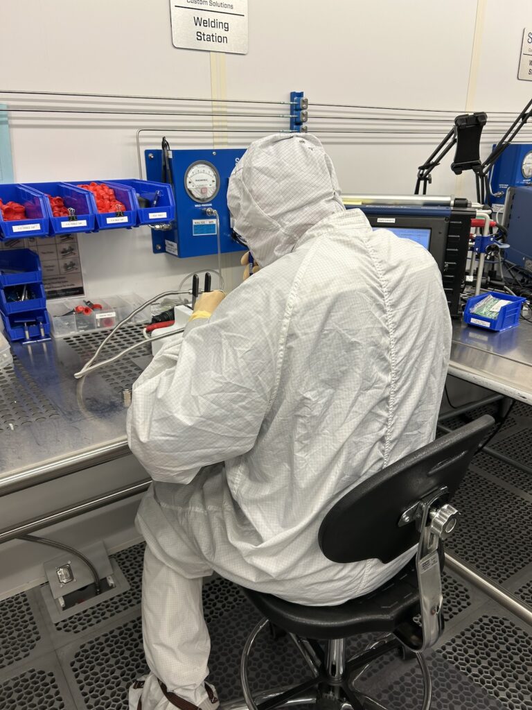 Rowan construction management program graduate Autie sits at a table wearing an all-white safety protocol outfit as he welds. 