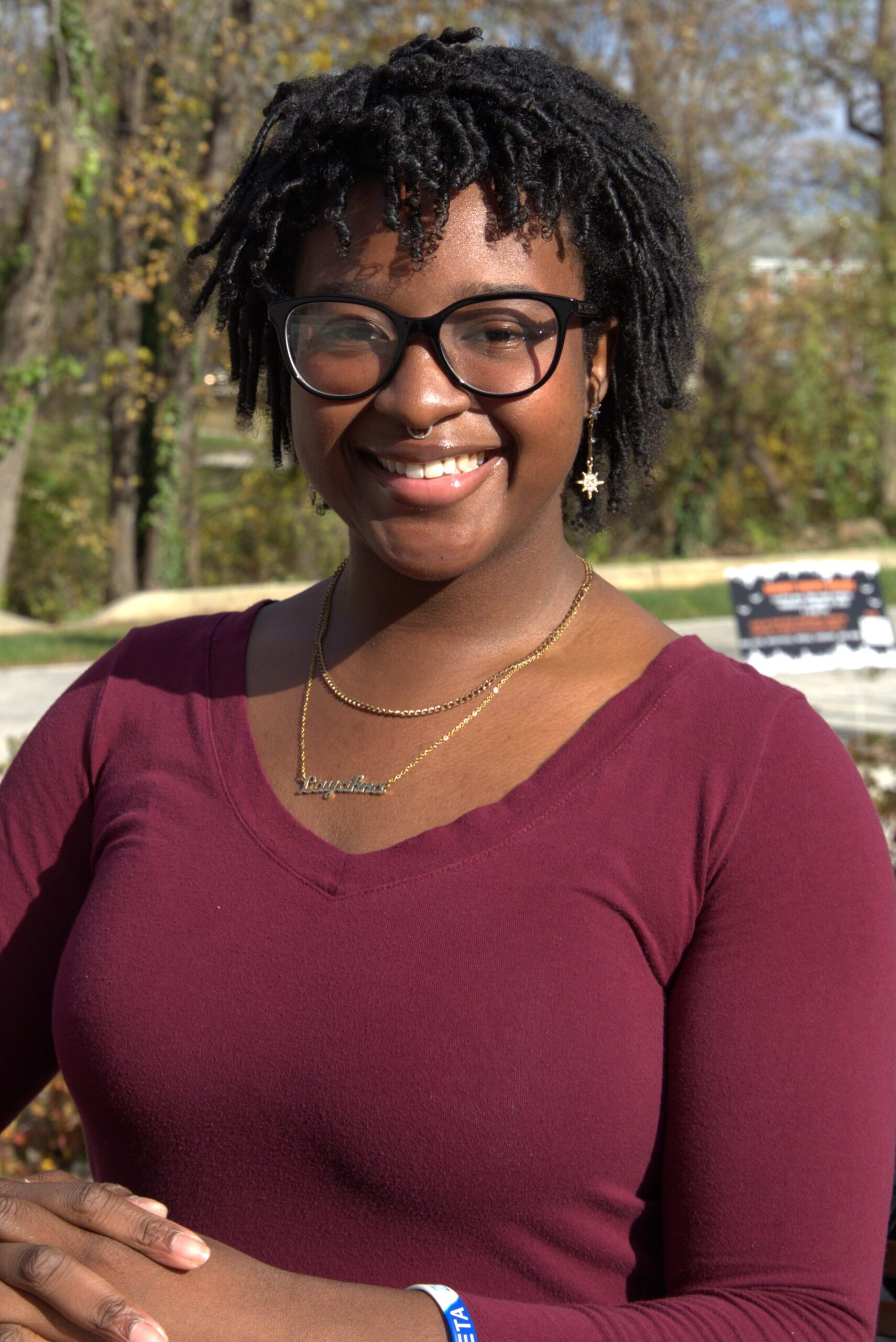 Rowan chemistry major Layahna sits for a formal portrait outdoors, smiling with her hands folded demurely in front of her. 