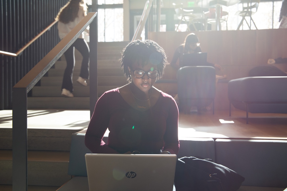 Rowan chemistry major Layahna sits in the student center studying on her laptop as filtered light streams across her face from the windows. 