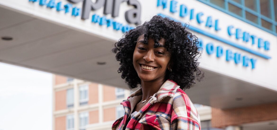 A Rowan MSN student stands in front of a medical center smiling.