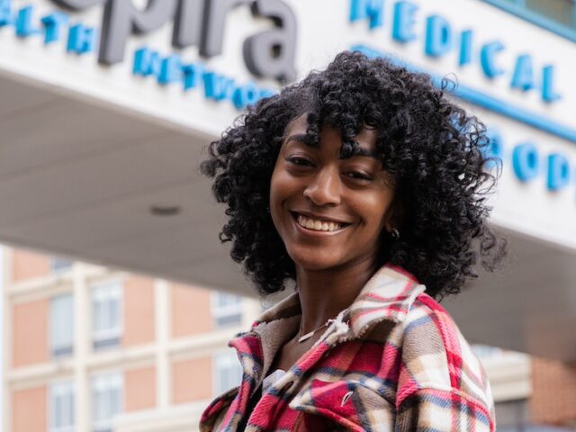 A Rowan MSN student stands in front of a medical center smiling.