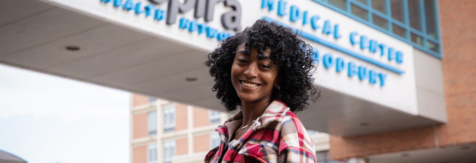 A Rowan MSN student stands in front of a medical center smiling.