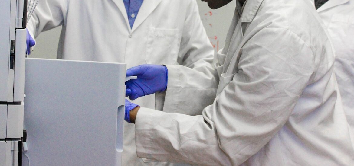 A close up of two chemistry students' hands as they place an item in equipment with a professor.