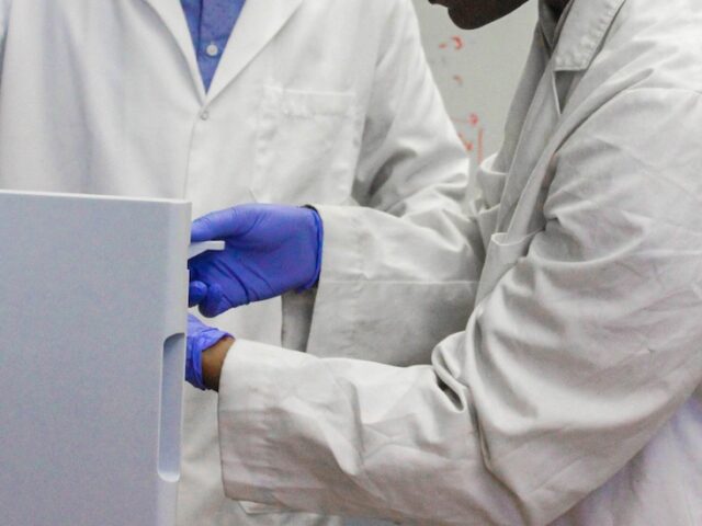 A close up of two chemistry students' hands as they place an item in equipment with a professor.