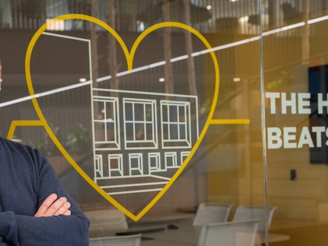 Standing in front of glass etched with the words "the heart of campus" a Rowan student stands smiling, his arms crossed in front of him.
