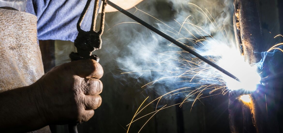 A stock photo image showing a close up of a construction management worker's hands as they weld an object.