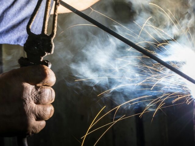 A stock photo image showing a close up of a construction management worker's hands as they weld an object.