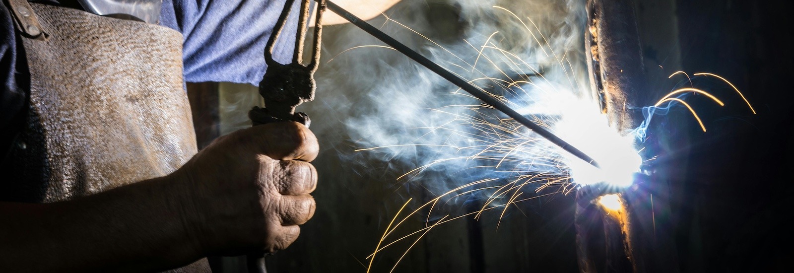 A stock photo image showing a close up of a construction management worker's hands as they weld an object.