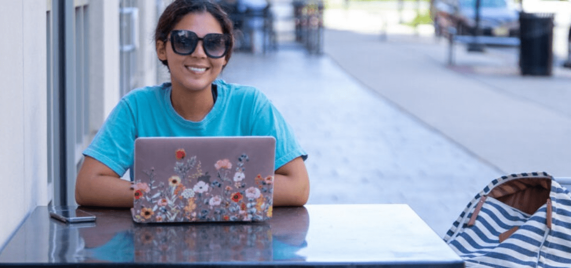 Student enrolled in college summer course completing work on laptop outside at table.