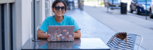 Student enrolled in college summer course completing work on laptop outside at table.