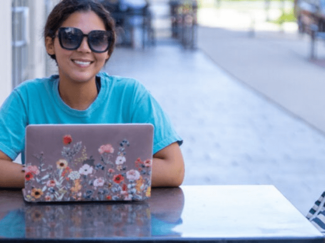 Student enrolled in college summer course completing work on laptop outside at table.