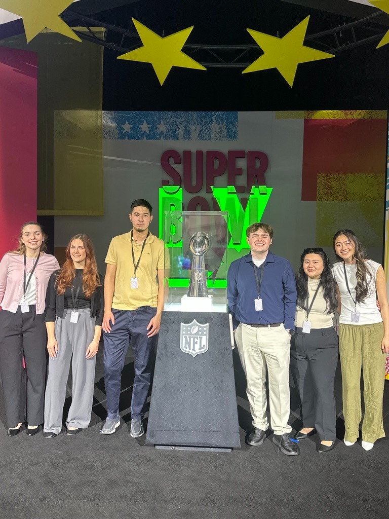 The six Rowan sports communication and media students pose beside the LX Super Bowl trophy during Super Bowl week ahead of the game. 
