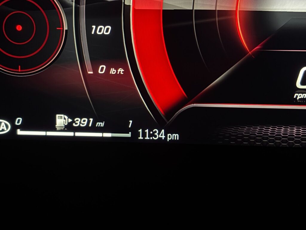 A close up of the black and red dashboard of Ryan's car, focused on the detail that it is 11:34 pm. 