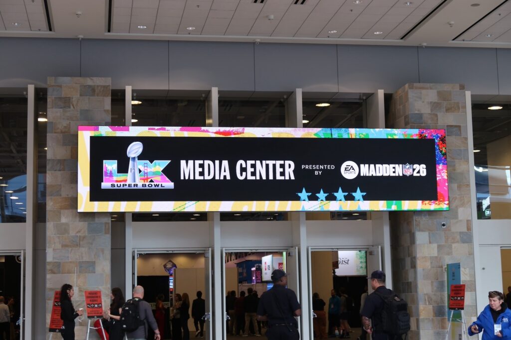 The signage above the convention center doors is lit up showing it is the LIX Super Bowl Media Center presented by Madden 26. 