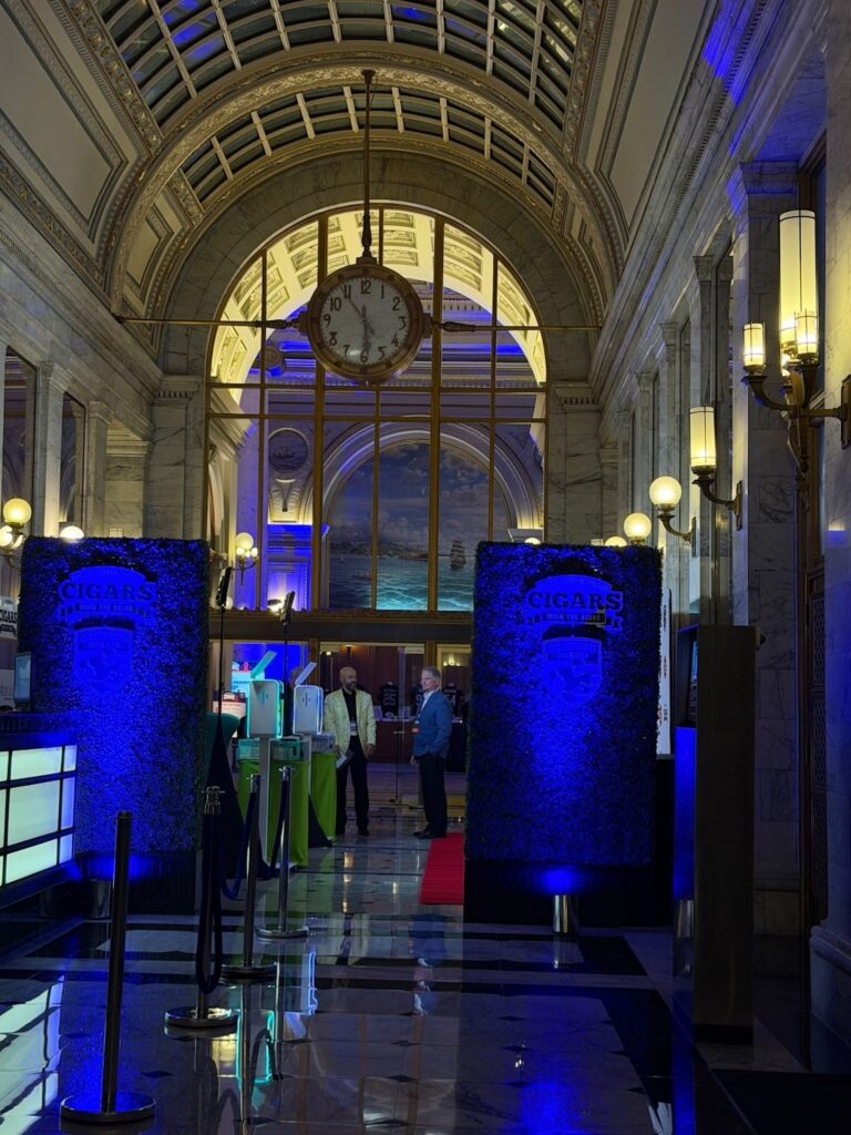 A dramatically lit entrance for Cigars with the Stars pre-Super Bowl event, with an arched hallway and event signage flanking the guest entrance. 