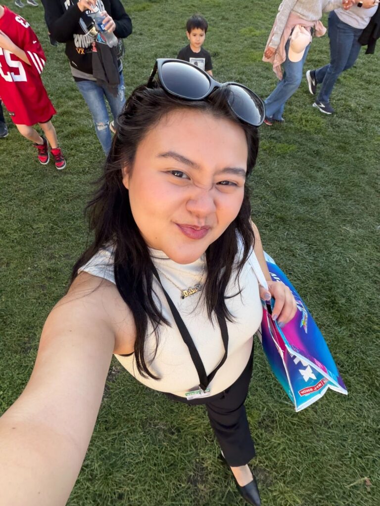 Julia scrunches her face for a happy expression taking a selfie from above, showing the grass beneath her feet. 