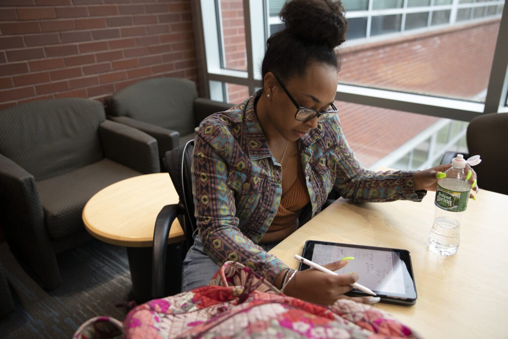 College student sitting at a table studying for finals on her tablet.