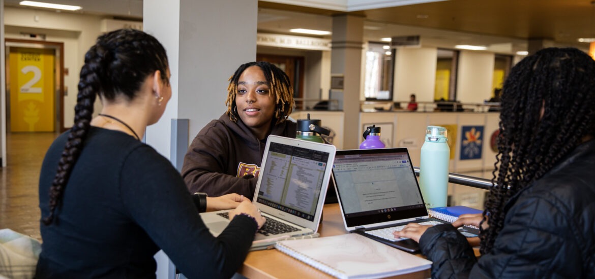 Three college students with laptops open collaborating and studying together to prep for end of semester finals.