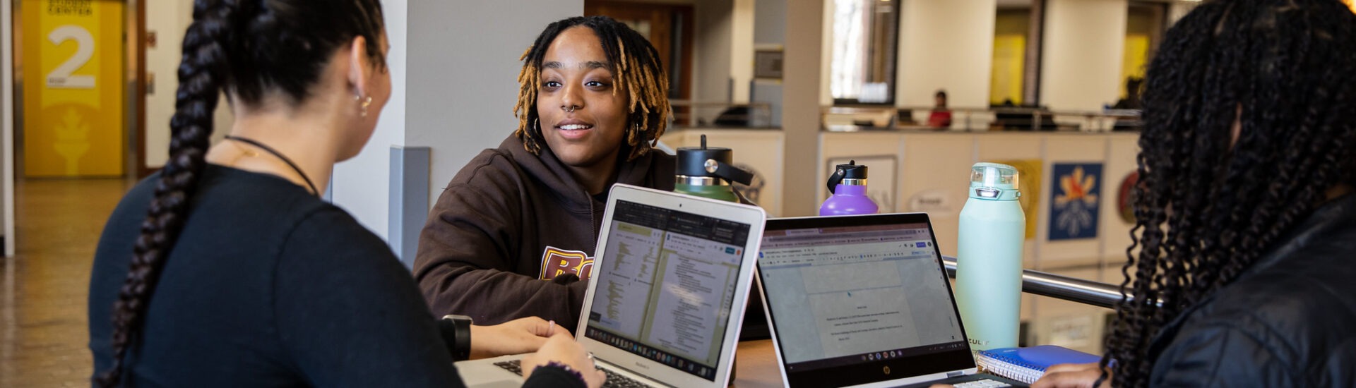 Three college students with laptops open collaborating and studying together to prep for end of semester finals.