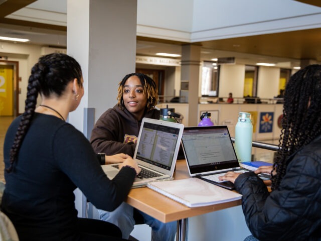 Three college students with laptops open collaborating and studying together to prep for end of semester finals.