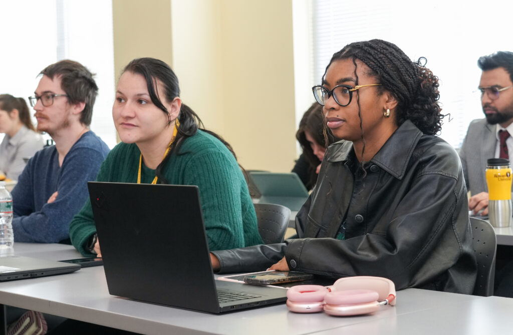 Rowan University students sit in a classroom with a laptop on the desk while listening and participating in a professional learning session.