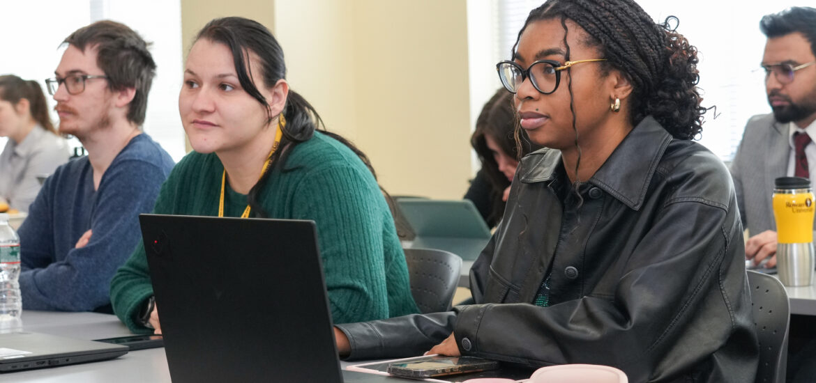 Rowan University students sit in a classroom with a laptop on the desk while listening and participating in a professional learning session.