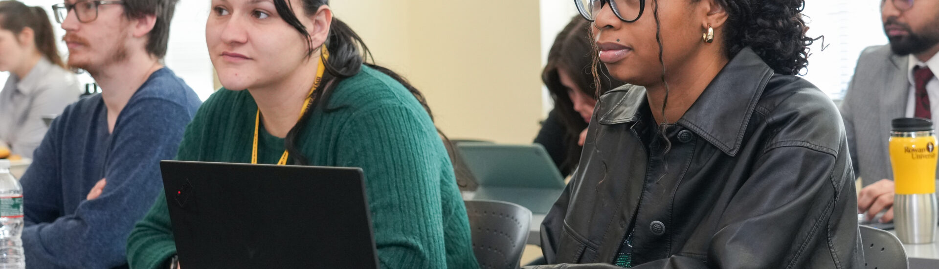 Rowan University students sit in a classroom with a laptop on the desk while listening and participating in a professional learning session.