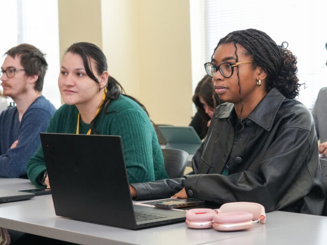 Rowan University students sit in a classroom with a laptop on the desk while listening and participating in a professional learning session.
