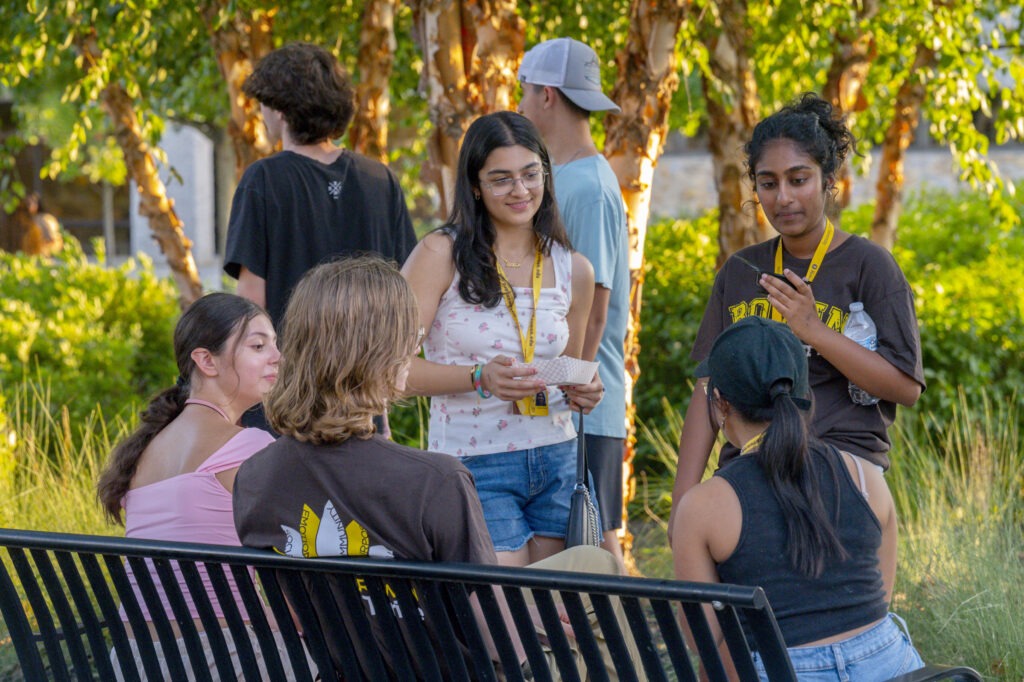 A group of Rowan University students sit and talk together on a bench during an outdoor campus food truck festival event.